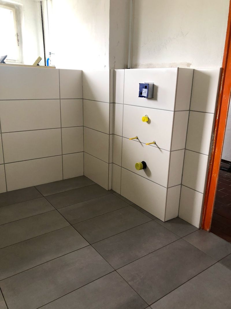 Badezimmer mit großformatigen grauen Bodenfliesen und weiß gefliester Vorwand